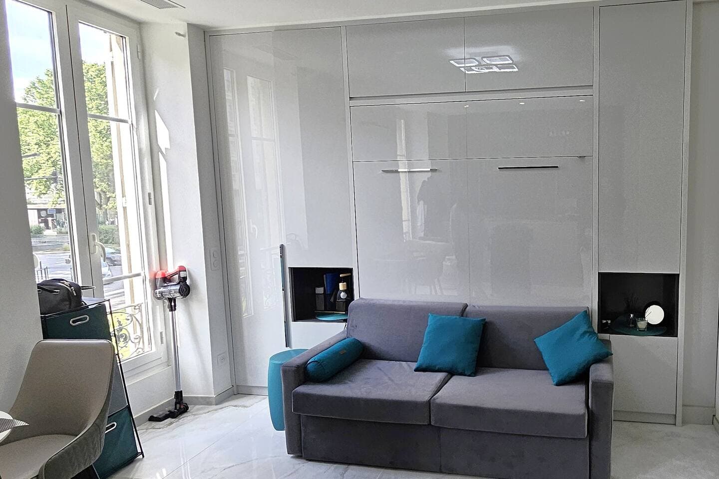Canapé gris et coussins turquoise devant une grande fenêtre du studio