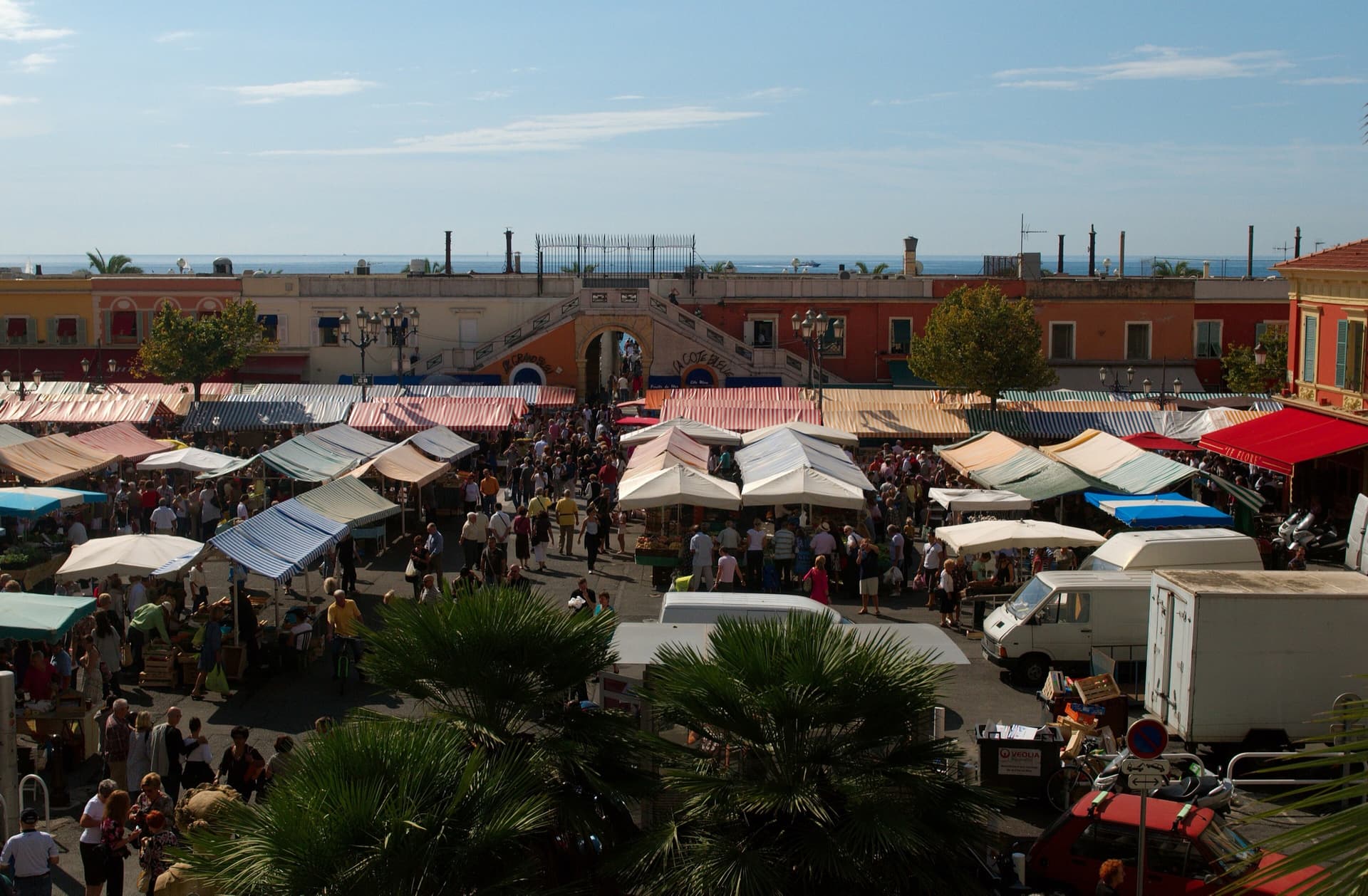 Le marche du cours Saleya dans le Vieux-Nice, ses etals sous les bannes rayees et la mer en arriere-plan.